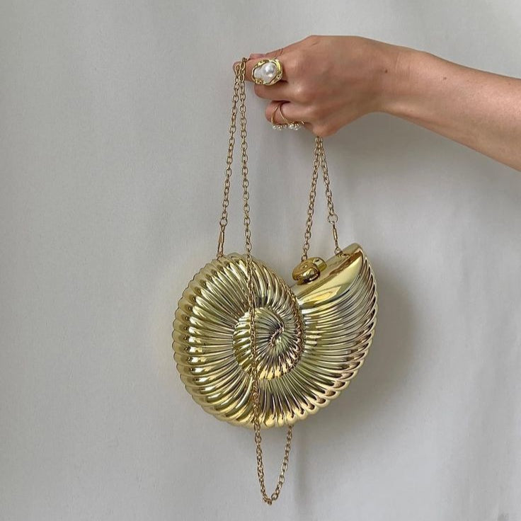 Gold shell-shaped handbag with a twist design, worn on a gold chain. Ideal for adding a unique touch to any outfit.