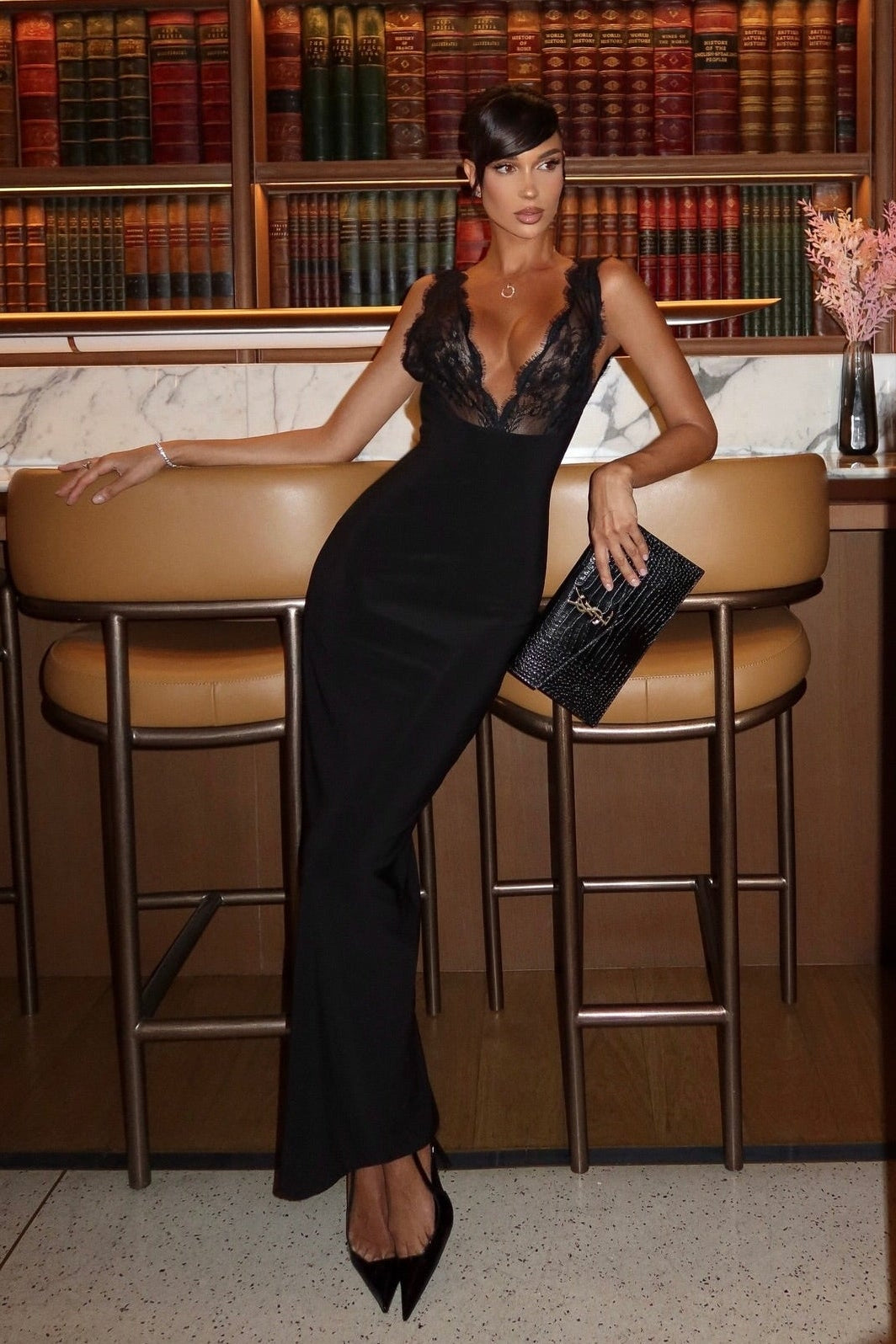Full-length view of black lace plunge neck maxi dress with hourglass silhouette, styled with clutch