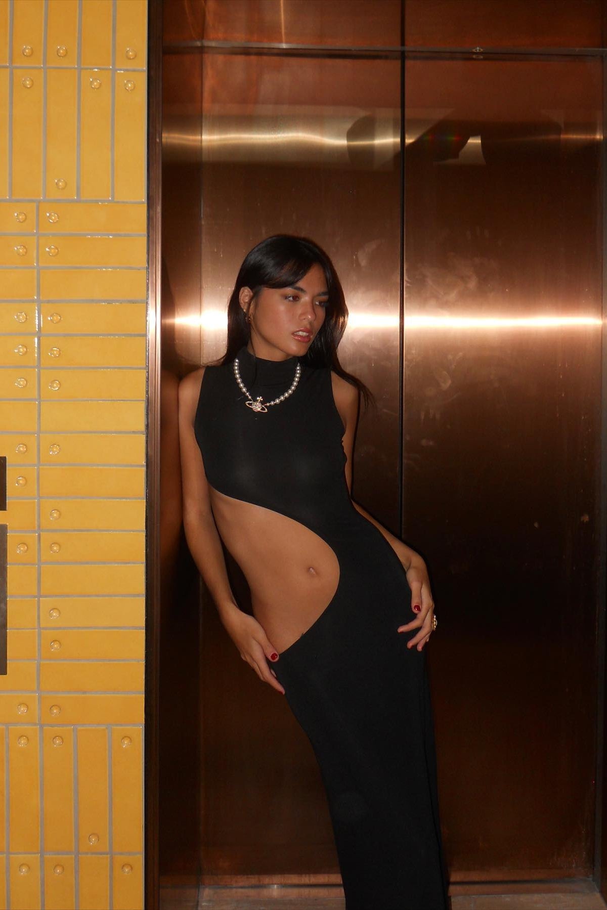 Woman in a black dress standing in an elevator with yellow walls.