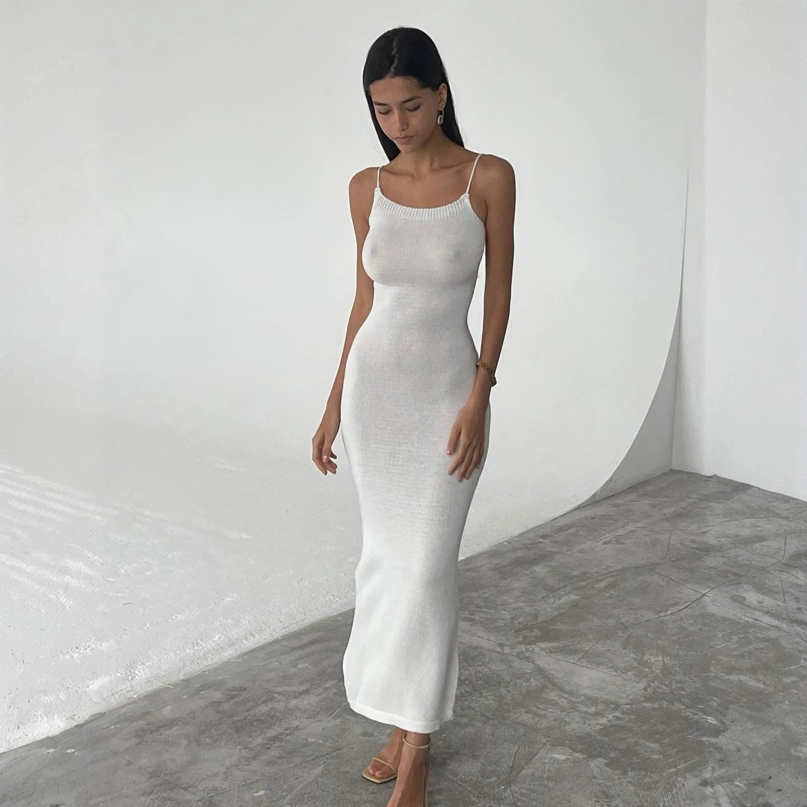 Woman wearing a white dress standing against a plain white wall.