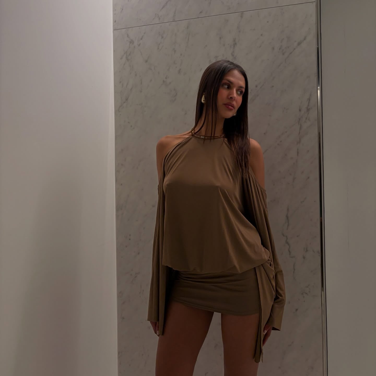 Woman wearing a brown outfit standing against a marble wall.