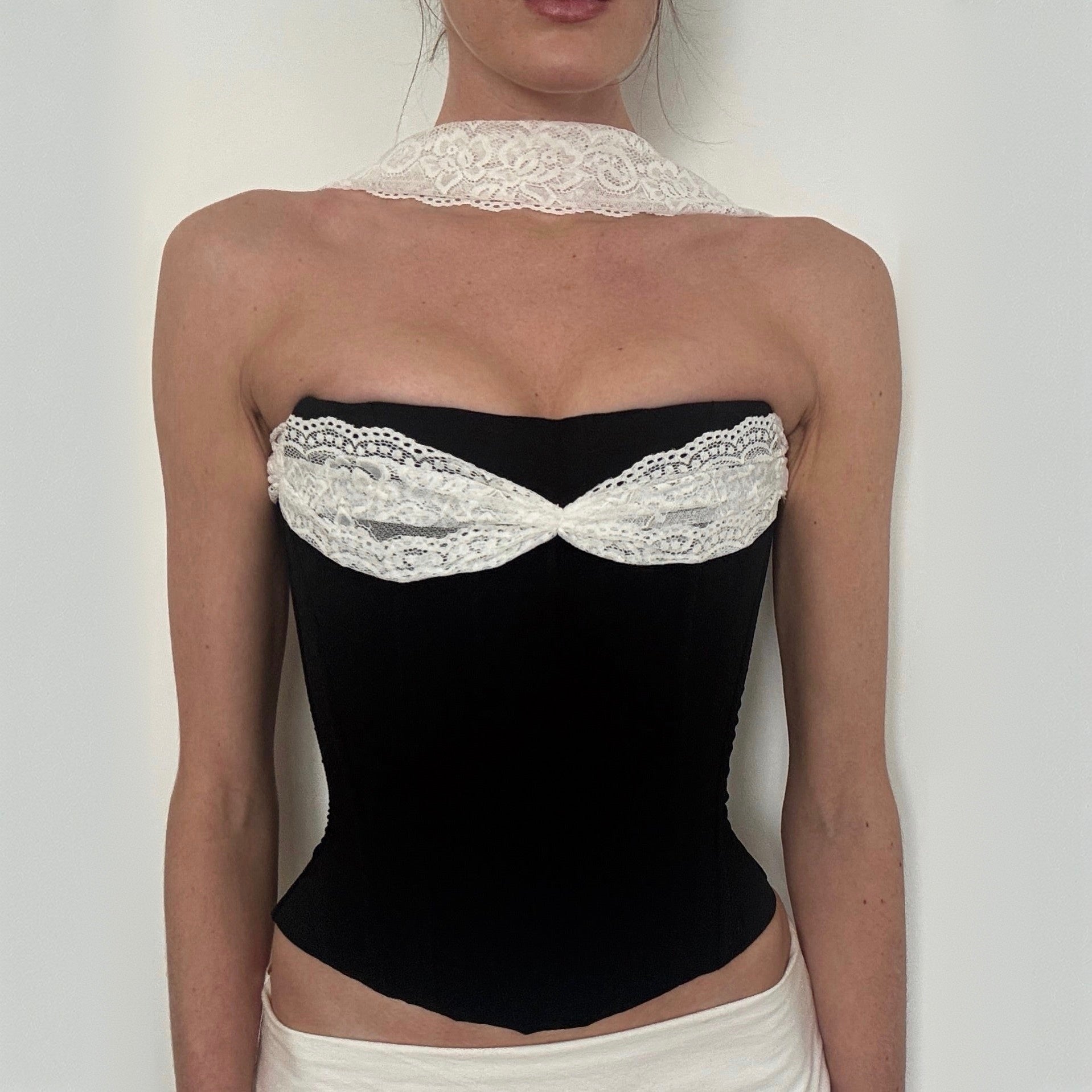 Black strapless top with white lace details worn by a person on a plain background