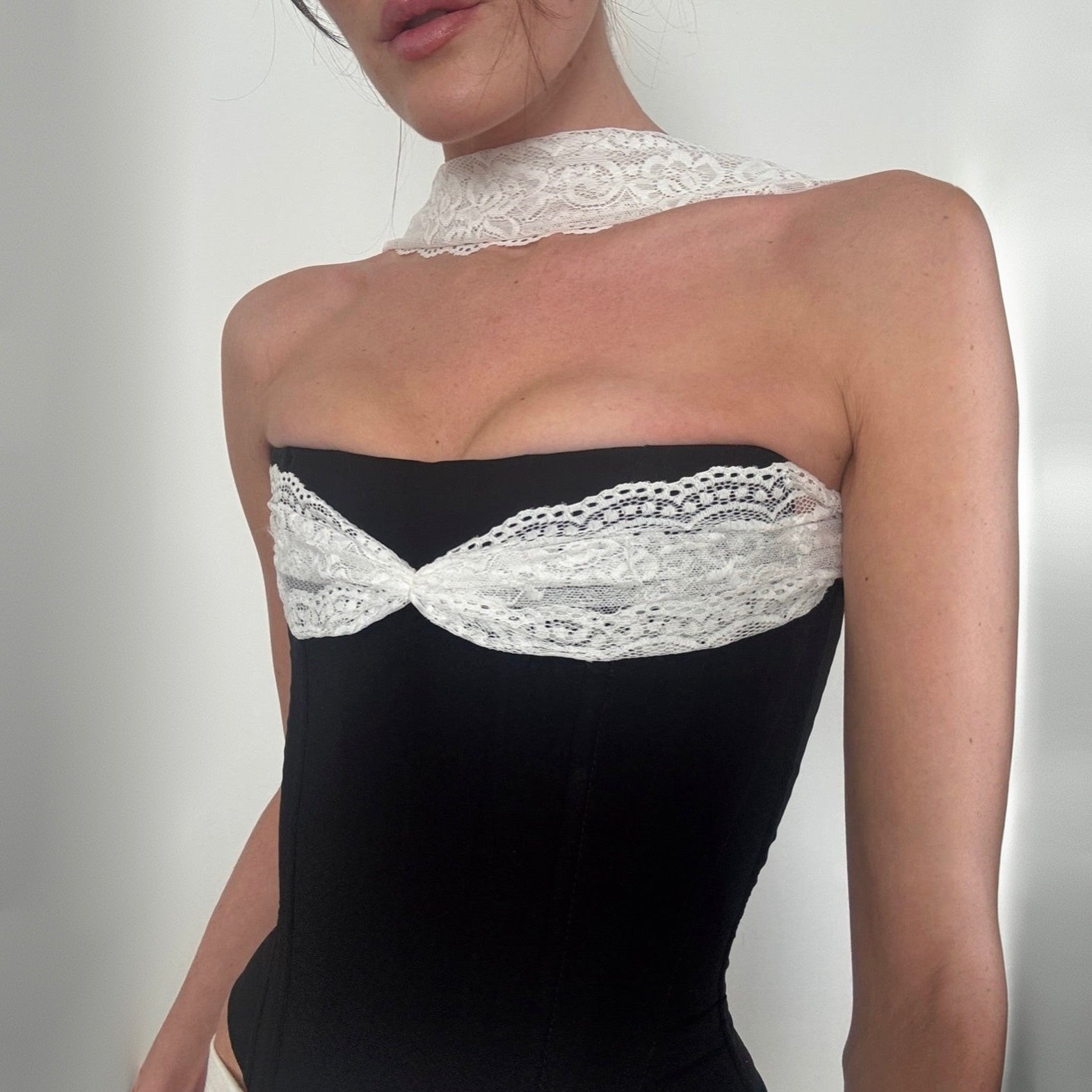 Black strapless dress with white lace details on a plain background