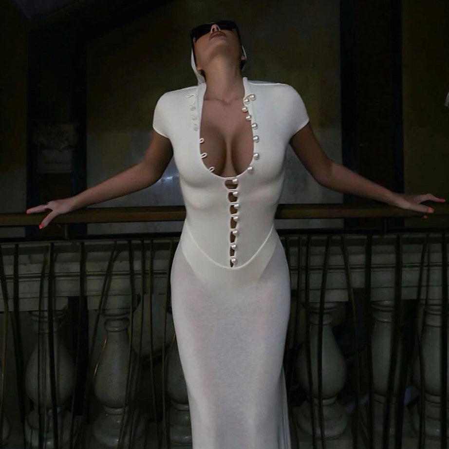 Woman in a white dress with a deep neckline and button details, standing on a balcony.