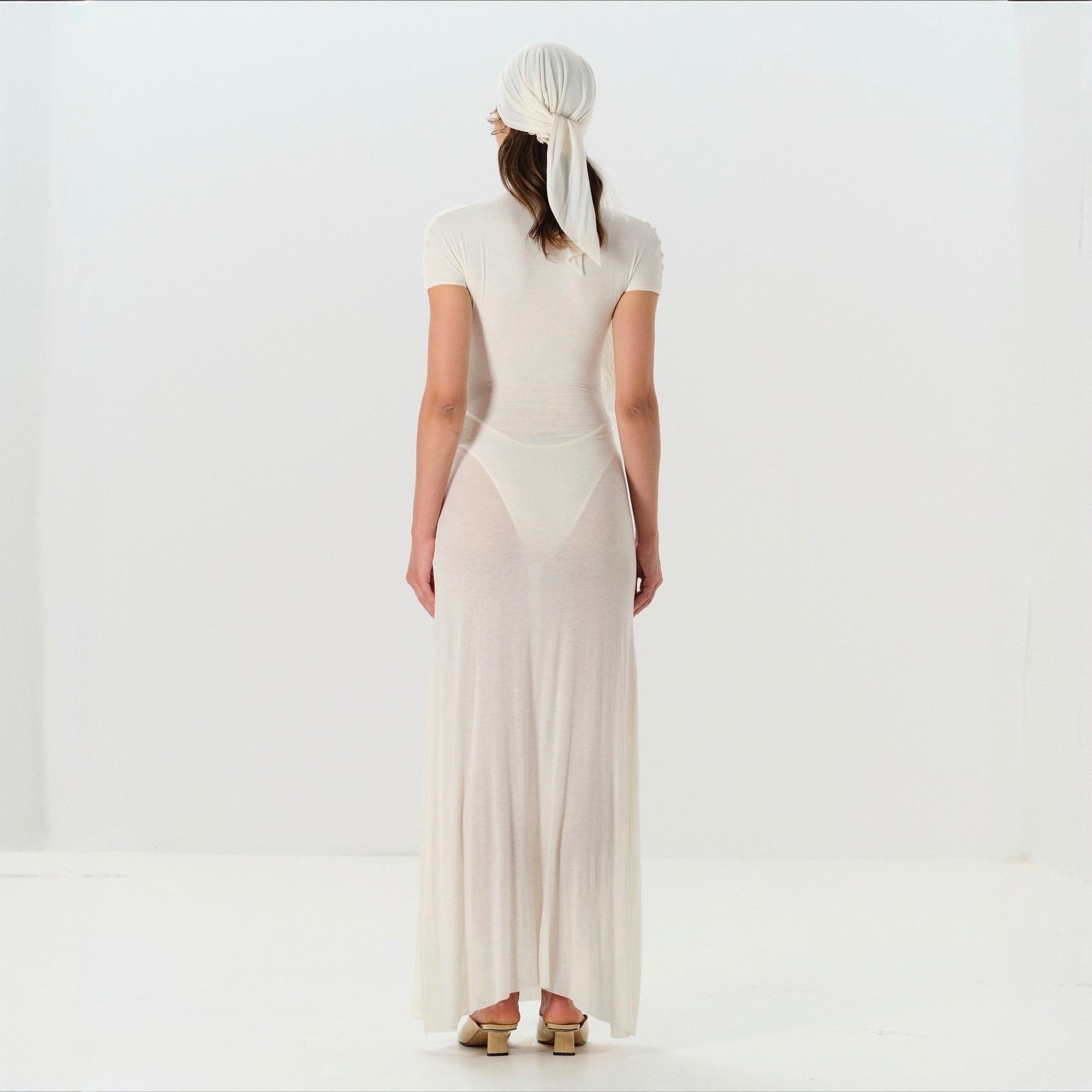 Woman wearing a white dress and headscarf on a plain background