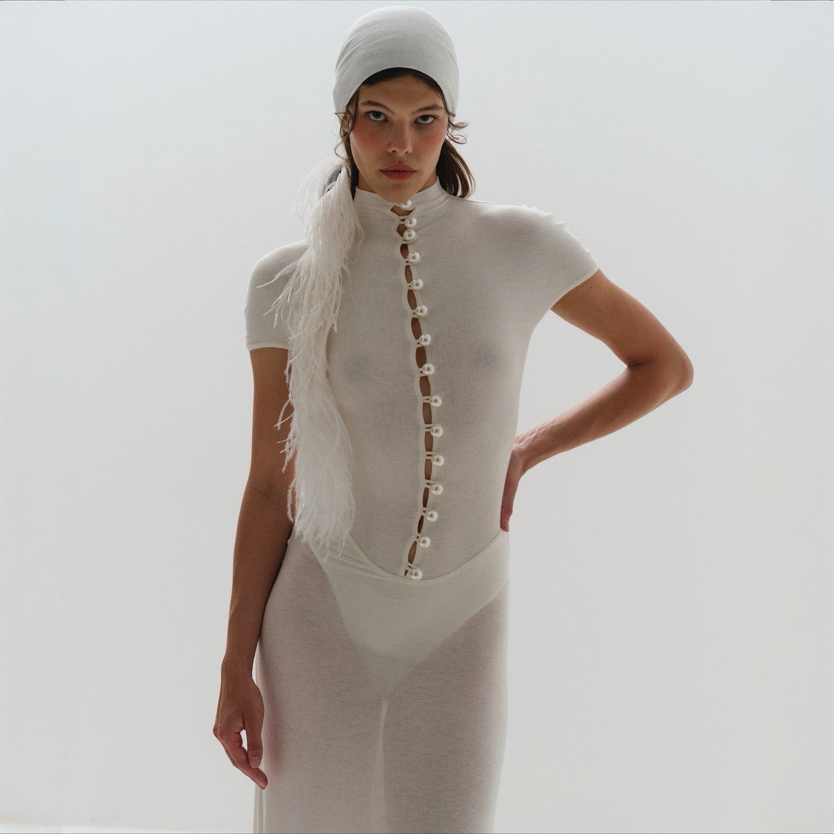 Woman wearing a white outfit with pearl details against a plain background
