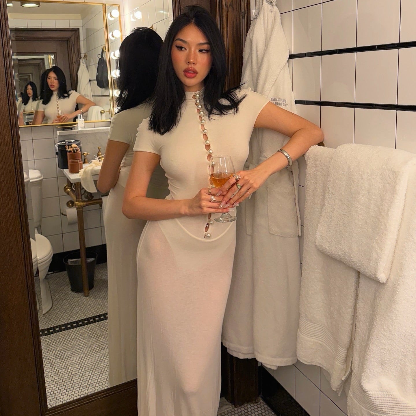 Woman in a white dress holding a glass in a bathroom