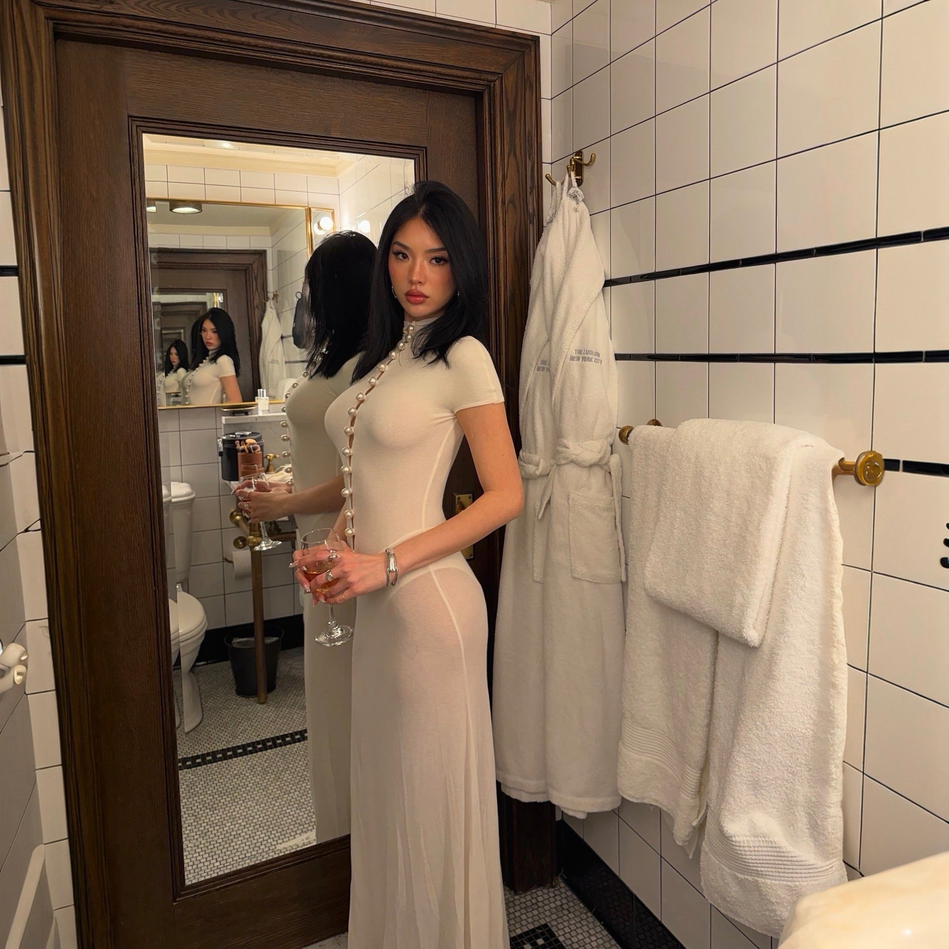 Woman in a white dress standing in a bathroom with towels and a robe.