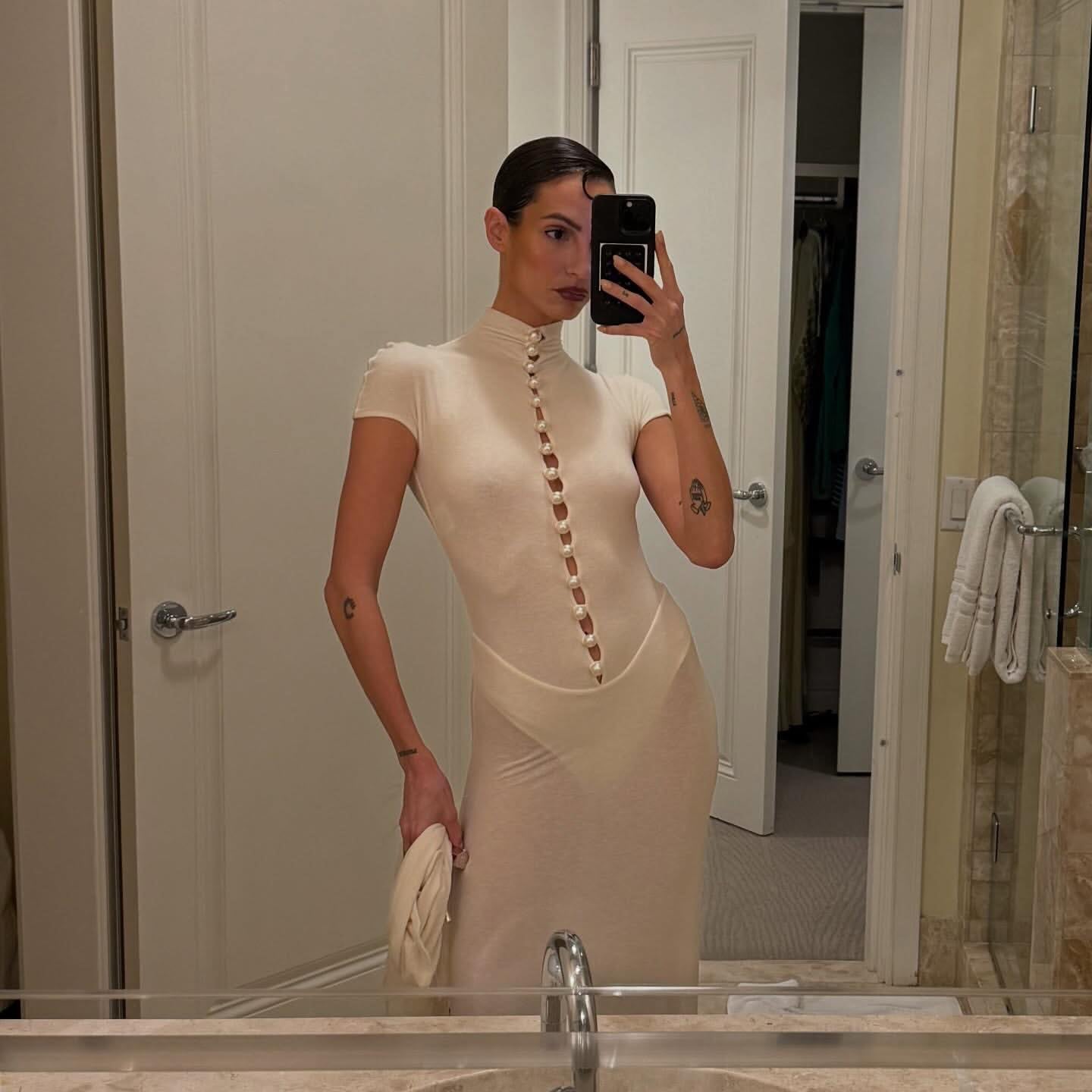Woman taking a mirror selfie in a beige dress in a bathroom.