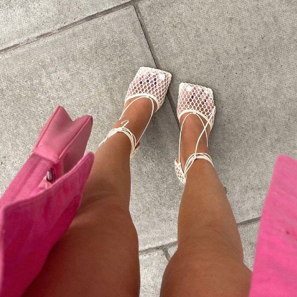 White mesh sandals worn on a gray pavement with pink shoes and bag visible.