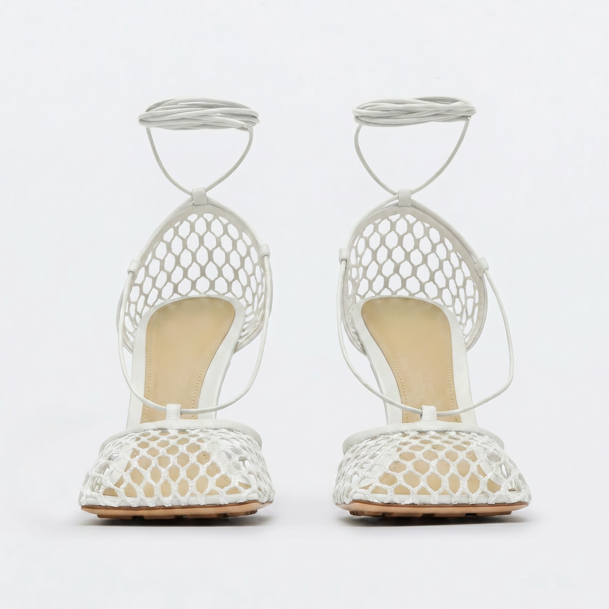 Pair of white high-heeled shoes with mesh design on a light gray background