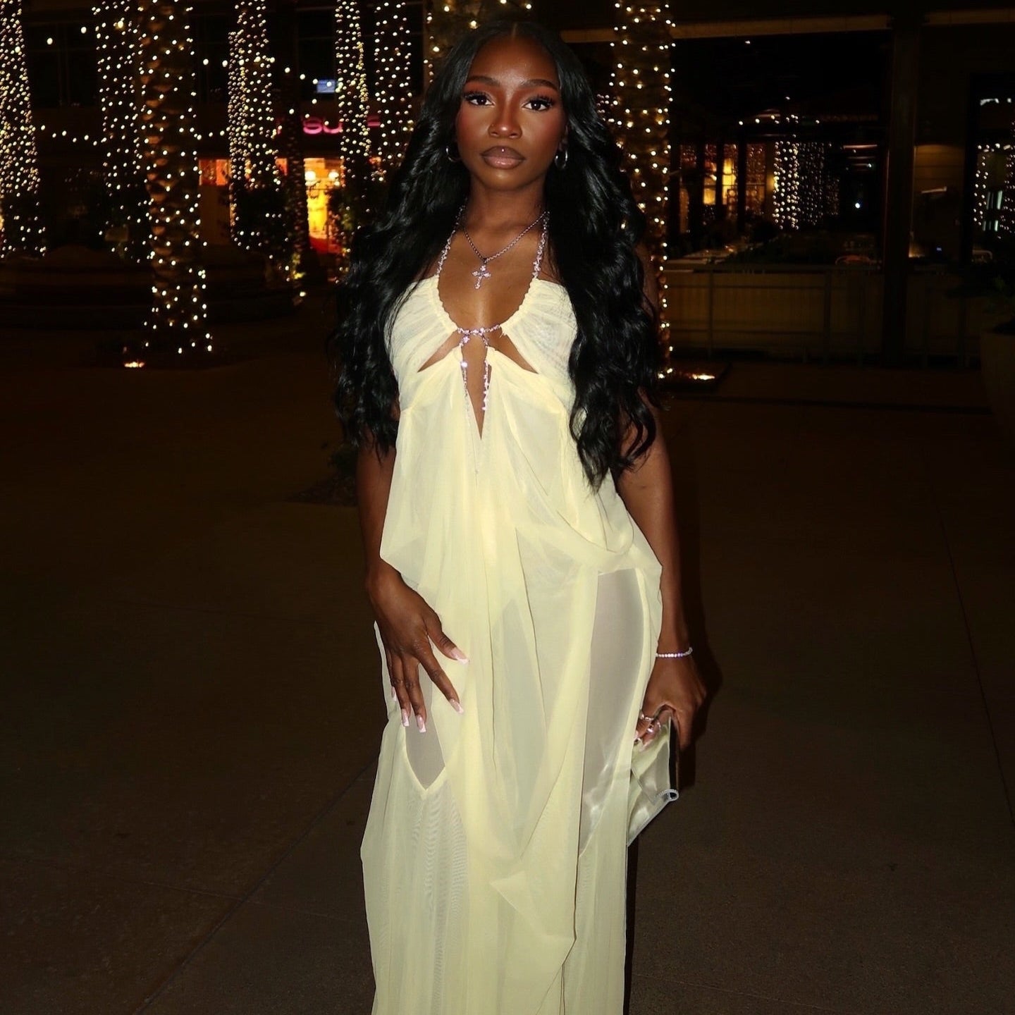 Woman in a white dress standing in front of illuminated palm trees at night.