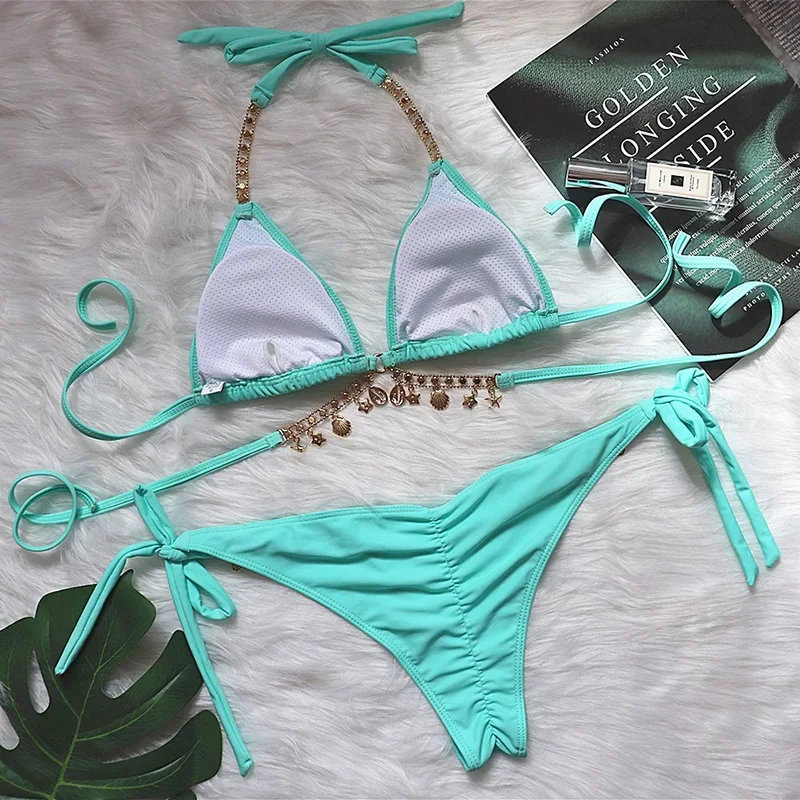Turquoise bikini set with decorative straps on a textured surface with a book and leaf.