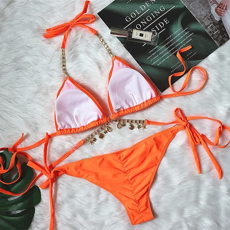 Orange bikini set with pink accents on a textured surface with a magazine and perfume bottle.