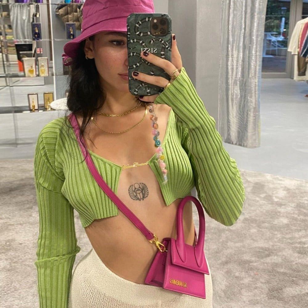 Person wearing a green ribbed sweater and pink hat, holding a pink handbag, in an indoor setting.