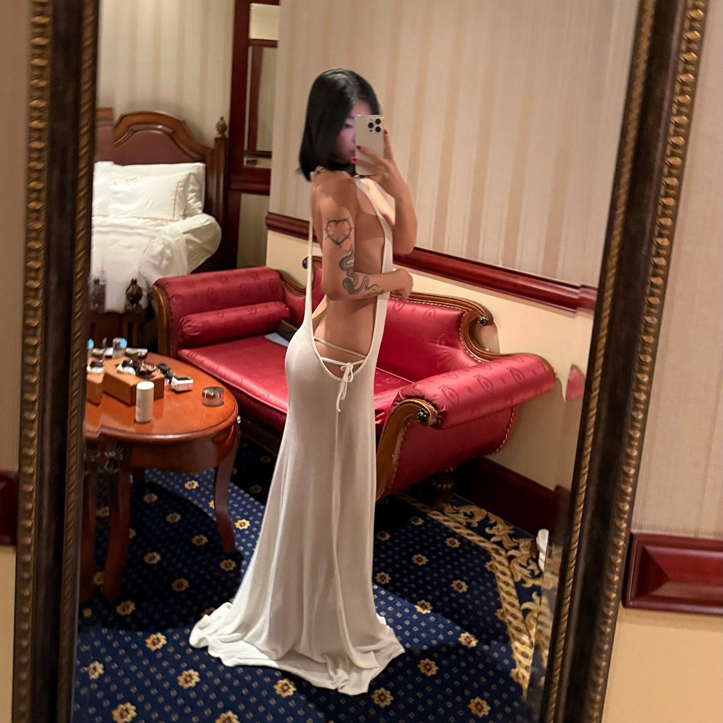Person in a white dress standing in a room with a red sofa and decorative rug.