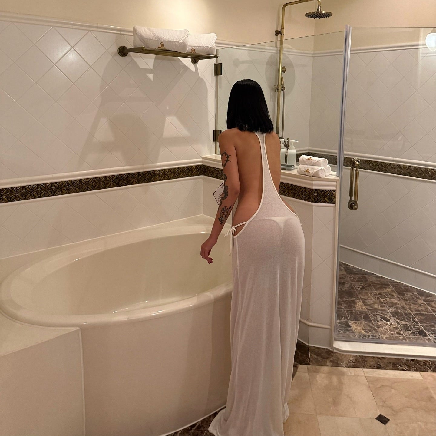 Woman in a white dress standing by a bathtub in a bathroom.