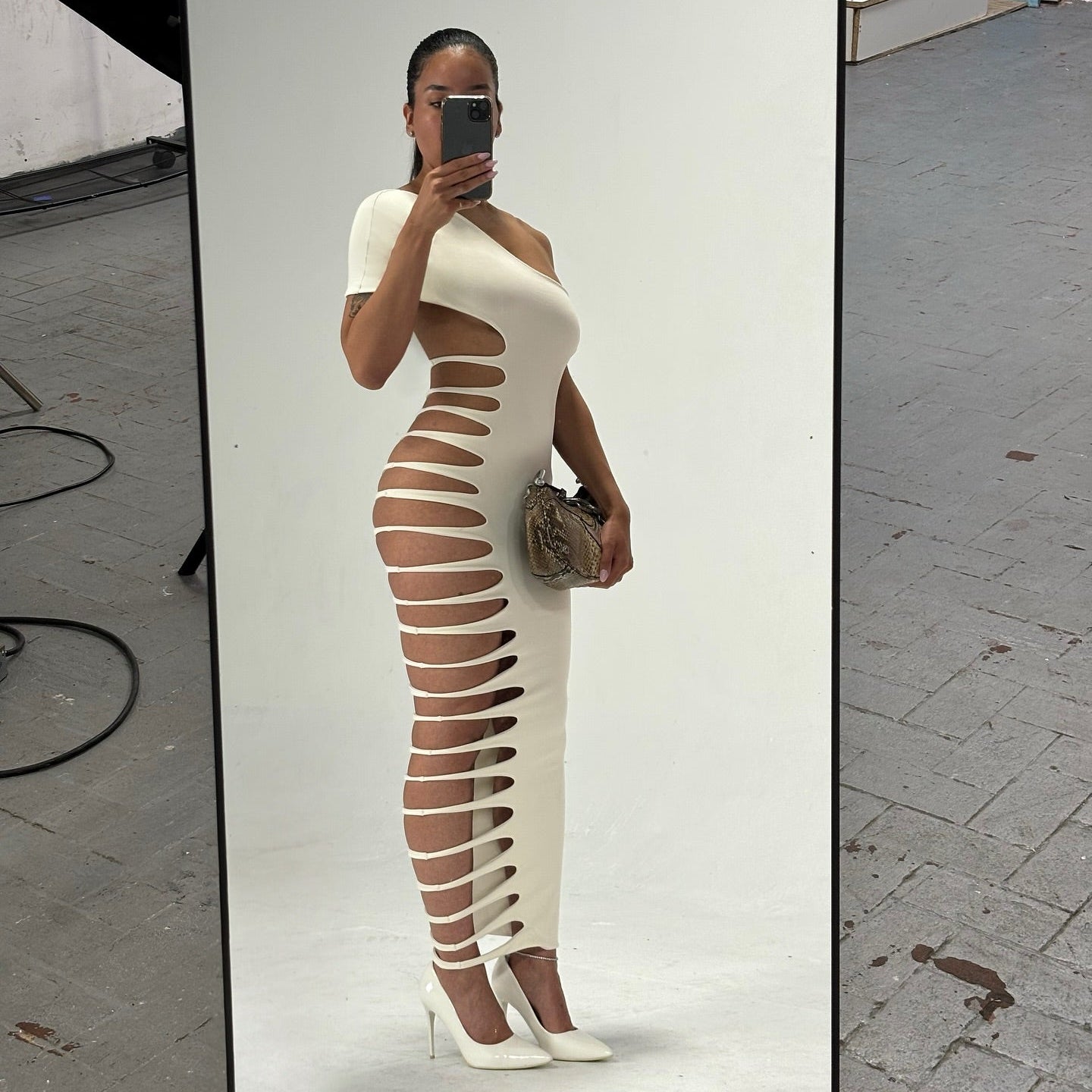 Person wearing a white dress with cut-out design in an urban setting.