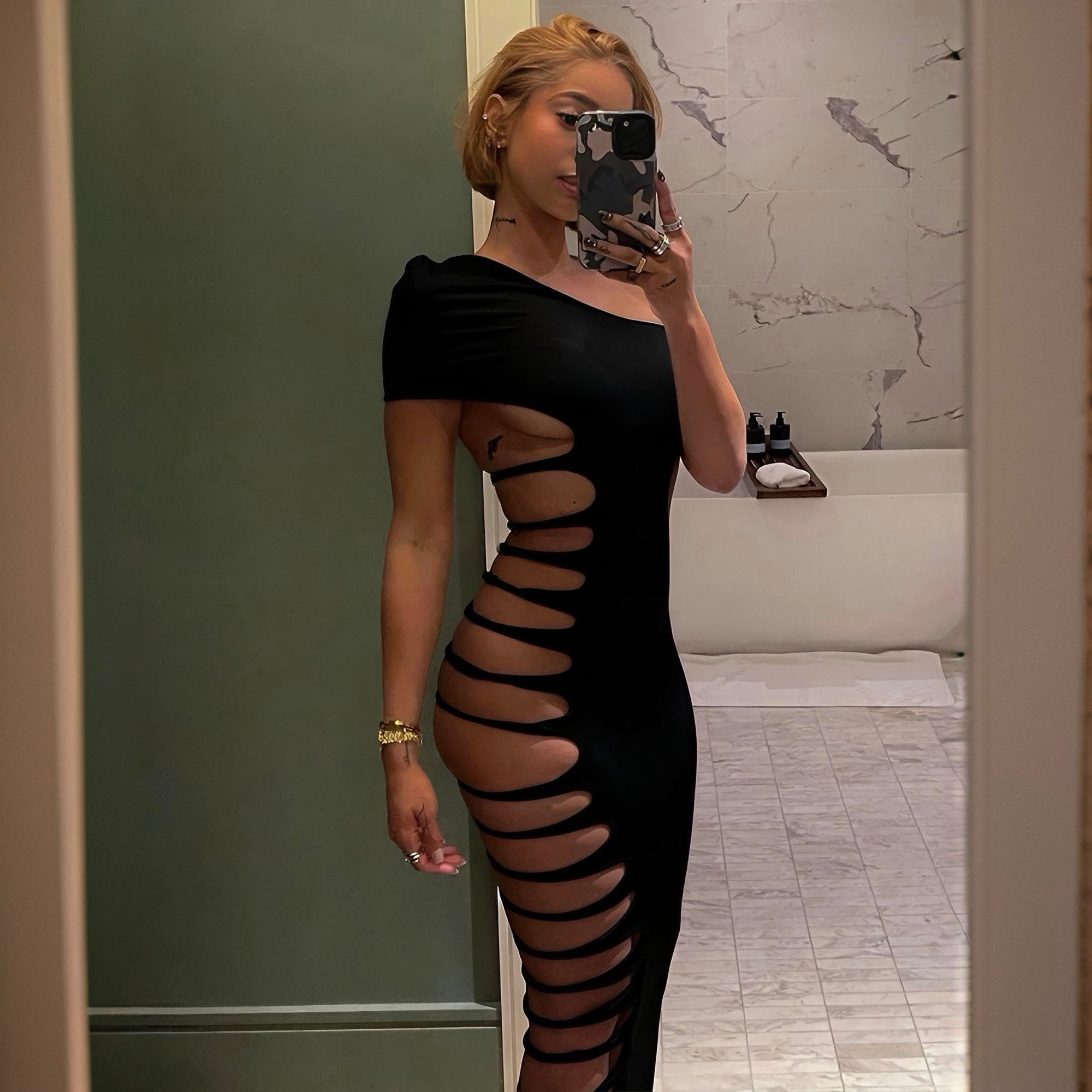 Woman wearing a black dress with cut-out design in a bathroom.