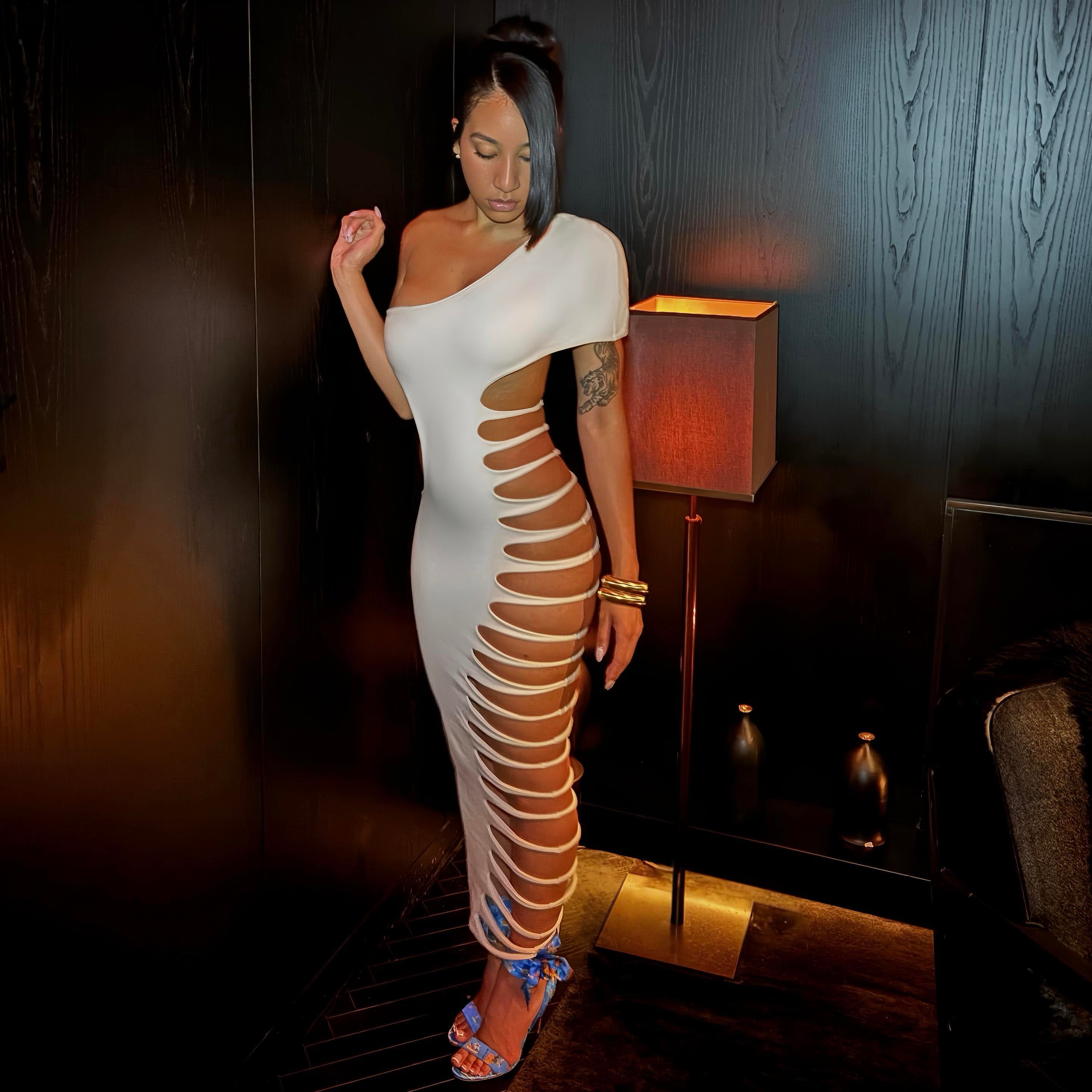 Woman wearing a white dress with cut-out design in a dimly lit room.