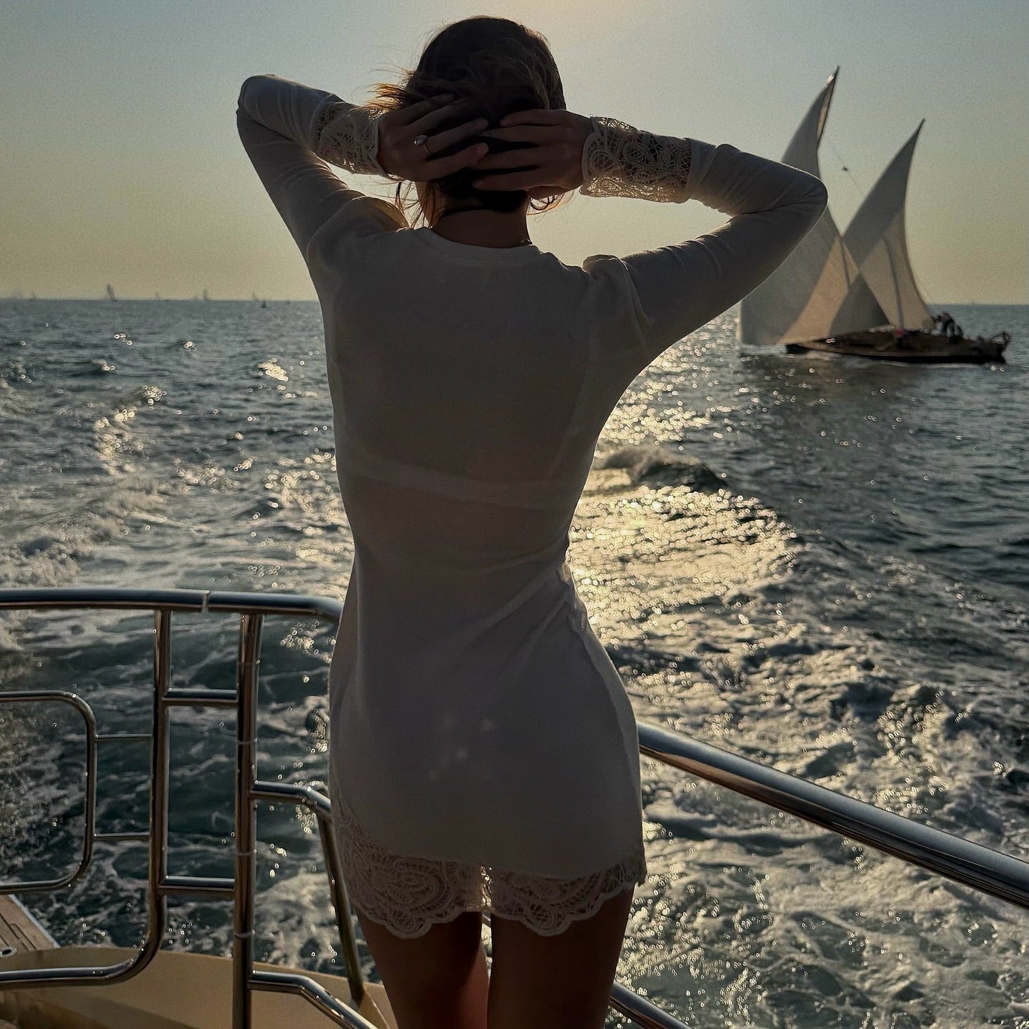 Woman on a boat looking at sailboats in the distance with the sun in the background