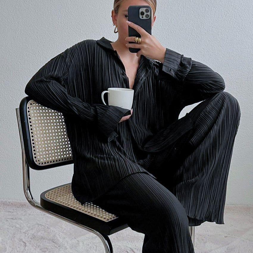 Person wearing a black pleated outfit sitting on a chair holding a white mug.