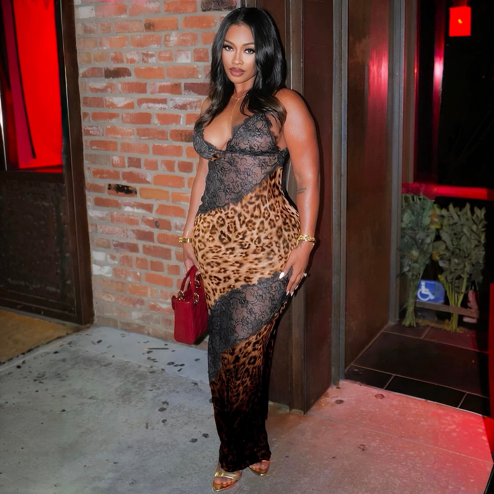 Woman in a leopard print and lace dress standing against a brick wall.