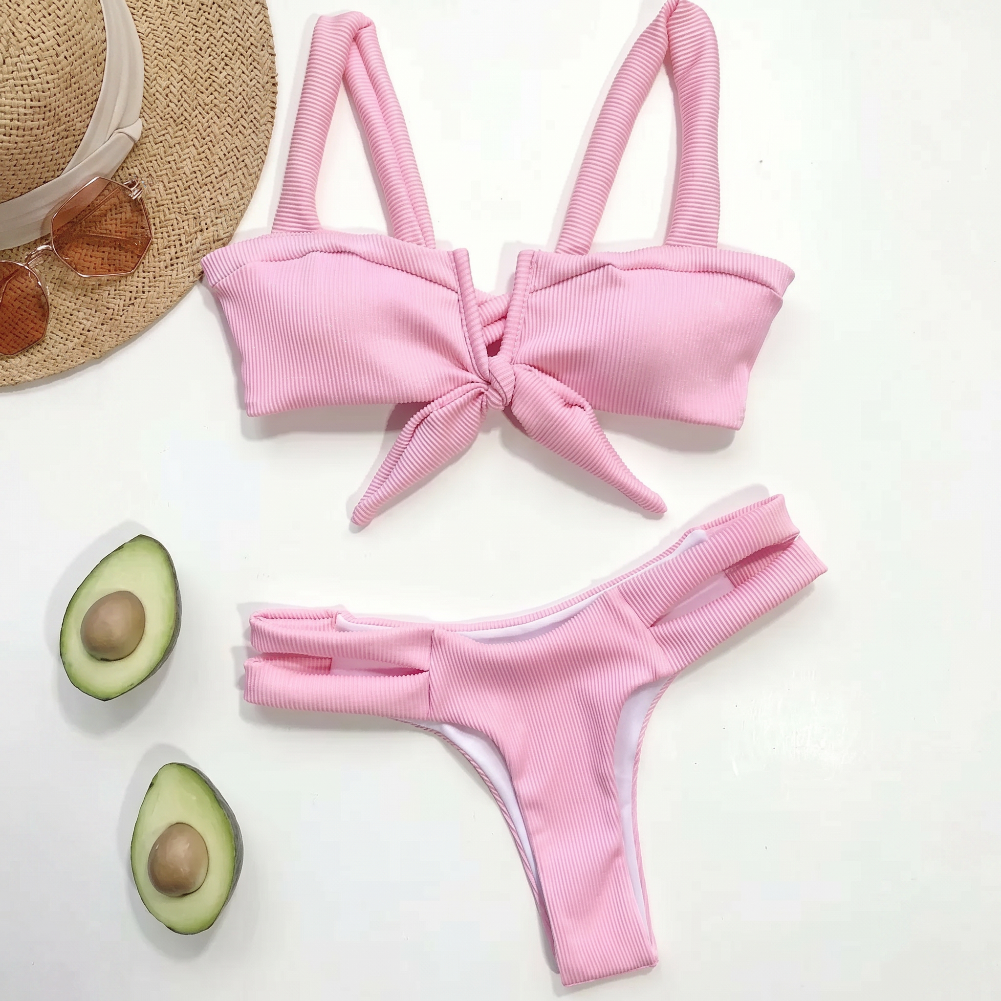Pink bikini set with a straw hat and avocados on a white background