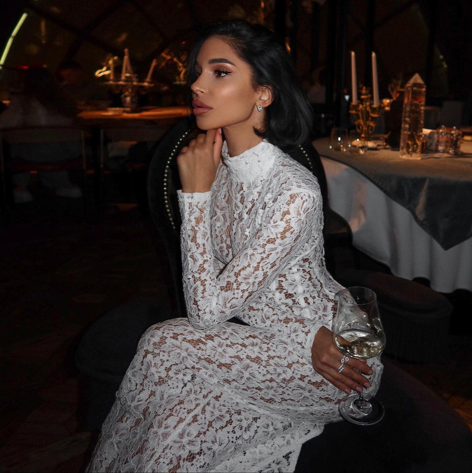 Woman in a lace dress holding a glass of wine in a dimly lit setting