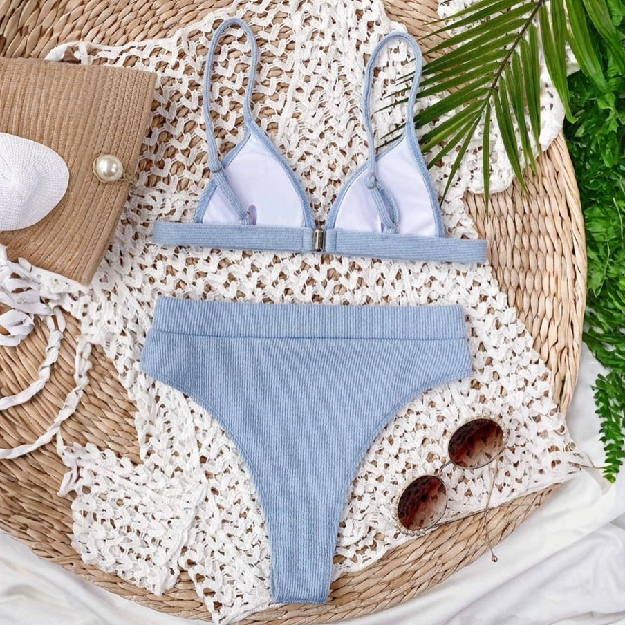 Blue bikini set on a textured surface with a woven mat and greenery.