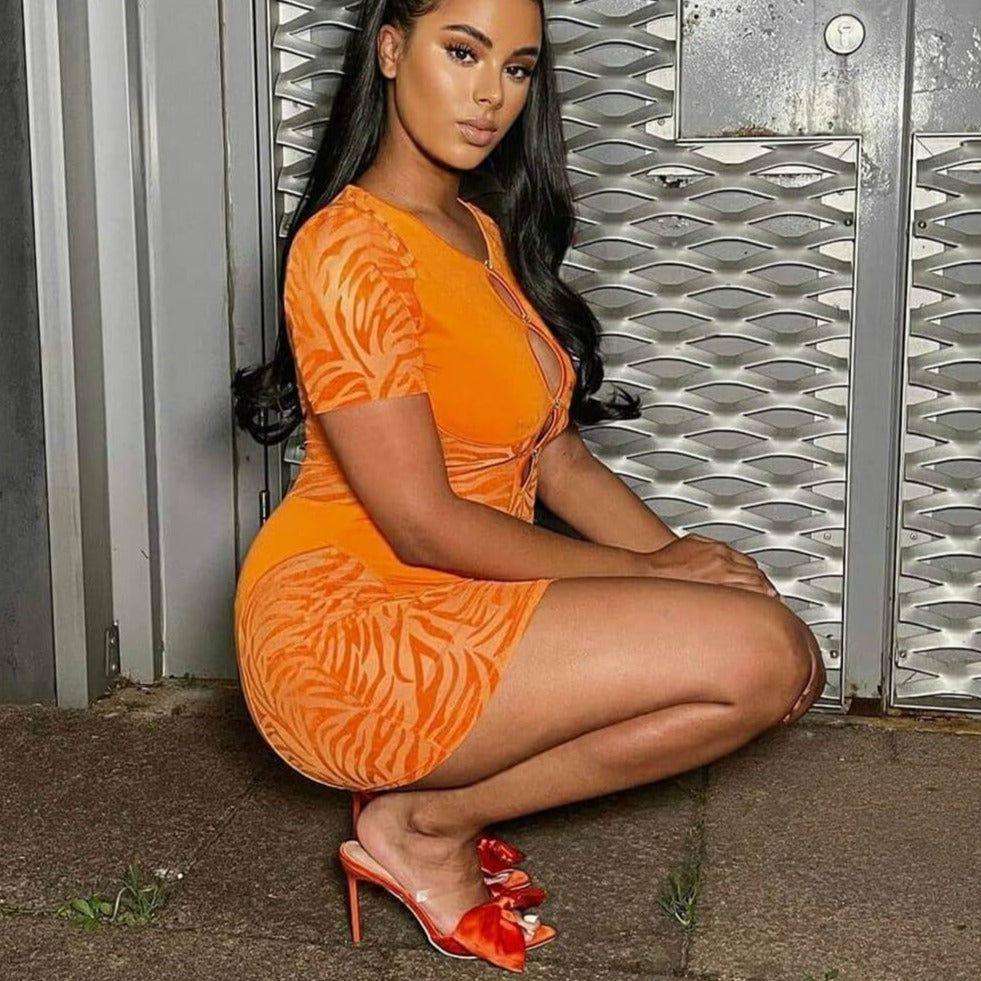 Woman in an orange dress sitting against a metallic wall.
