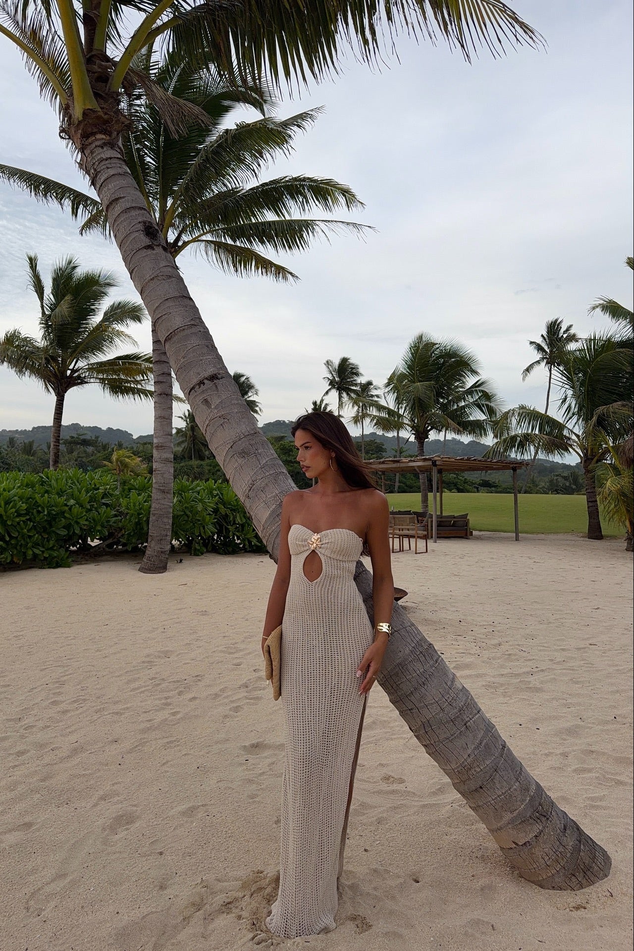Full-length ivory knit cut-out maxi dress on model by palm tree, fitted strapless silhouette