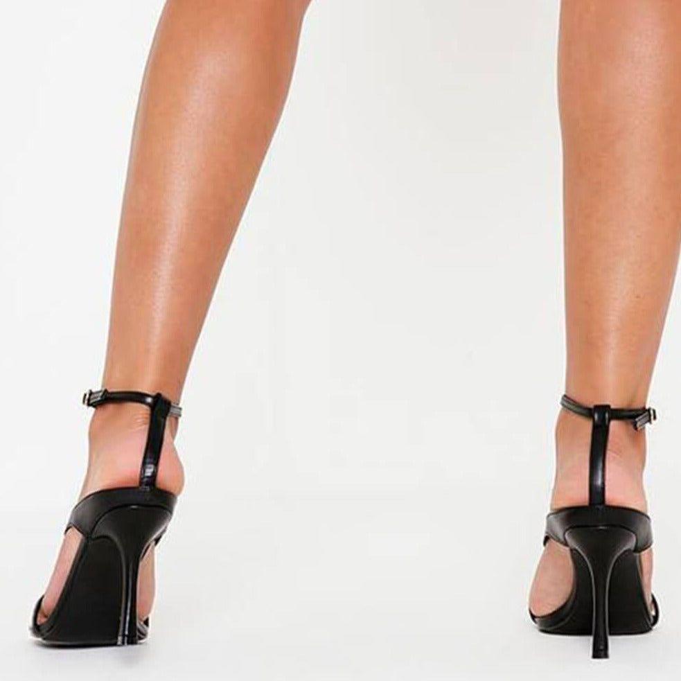 Black high-heeled shoes worn by a person on a white background