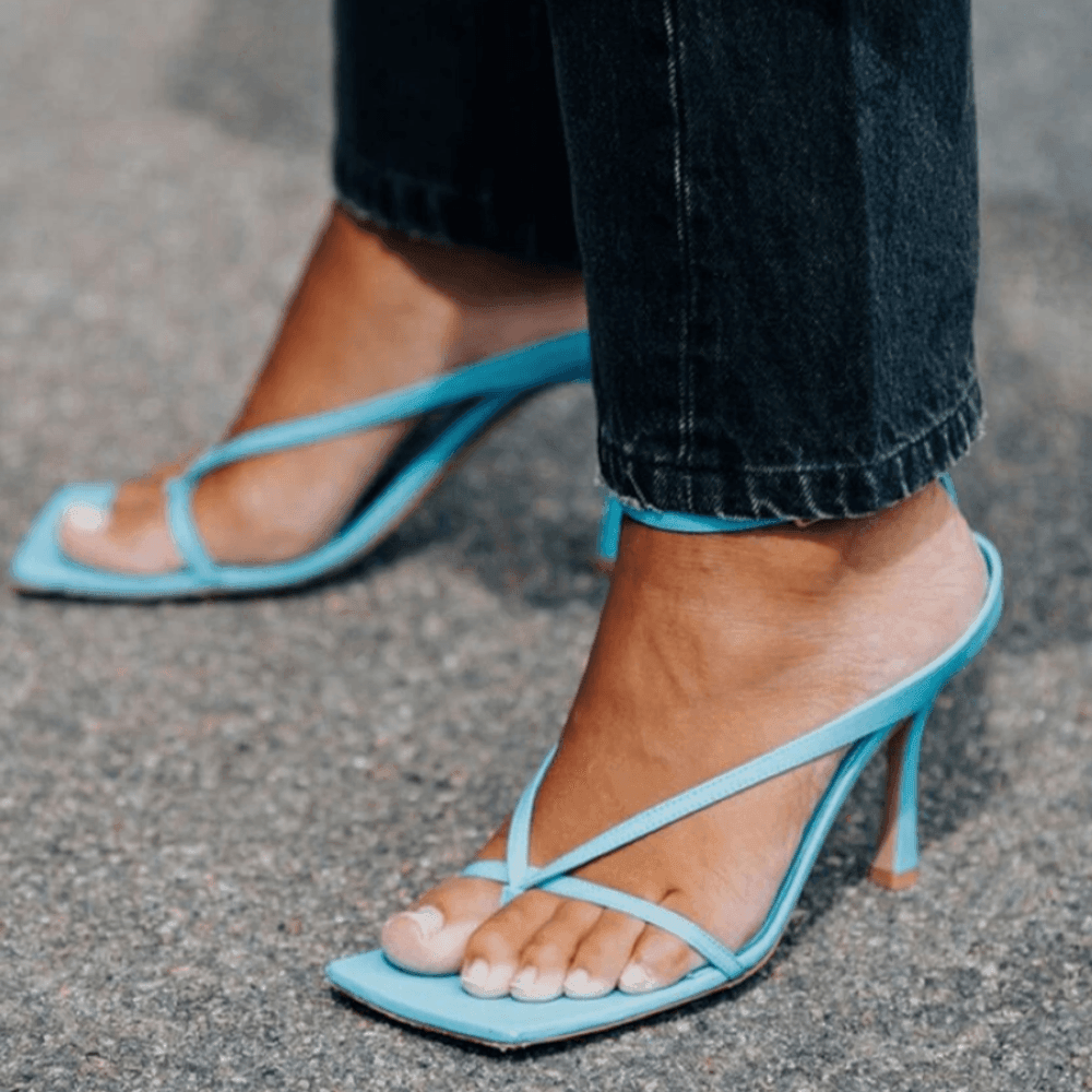 Light blue high-heeled sandals worn with dark jeans on a gray pavement.
