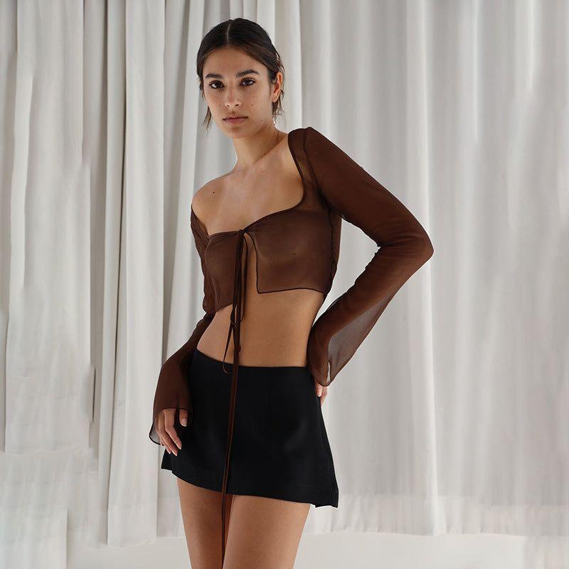 Woman wearing a brown top and black skirt against a white curtain background