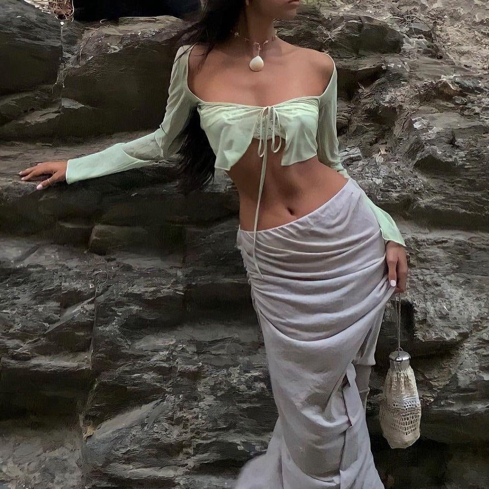 Woman in a light green top and white skirt standing against a rocky background