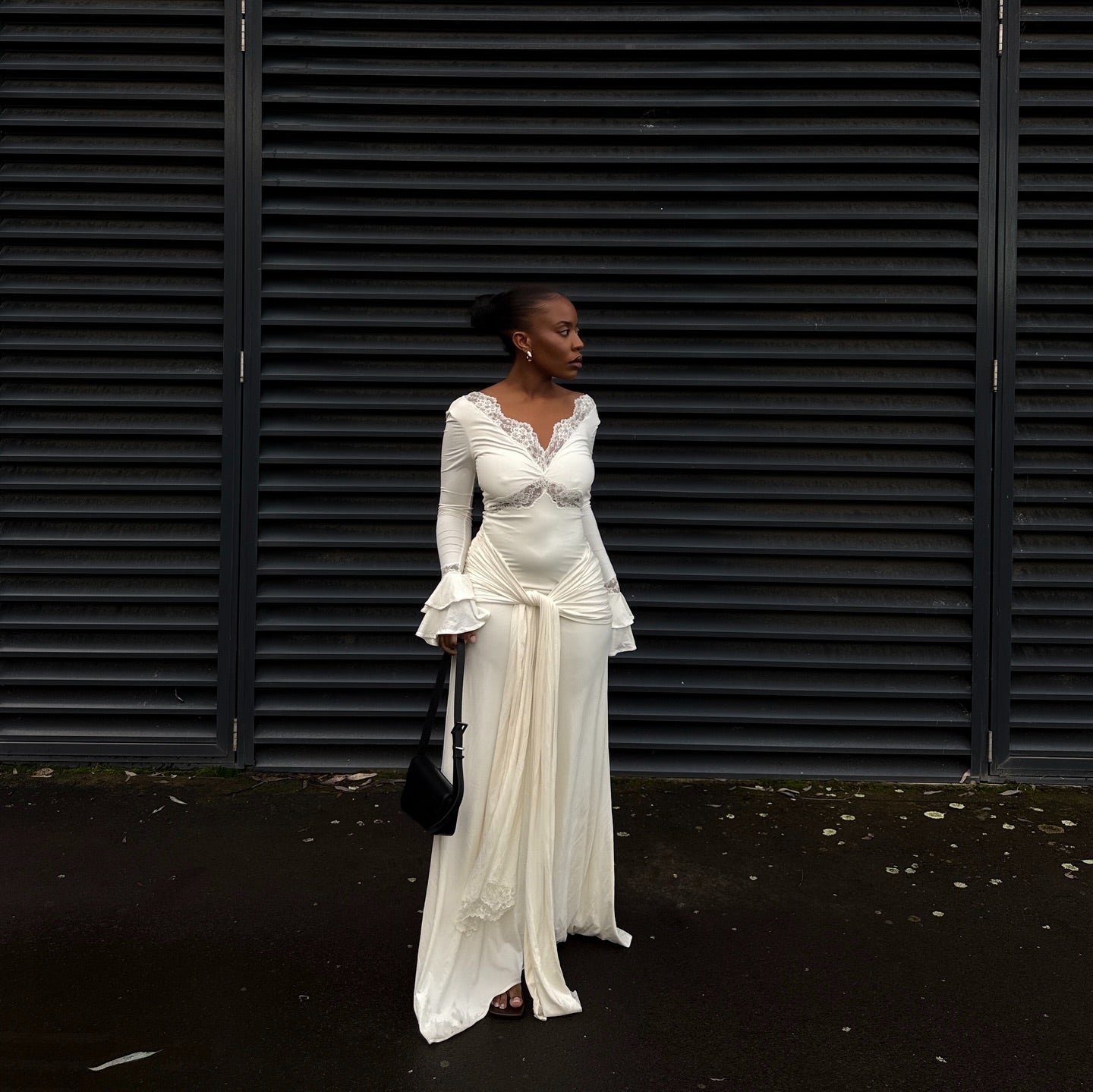 Woman in a white dress standing against a black shuttered wall.