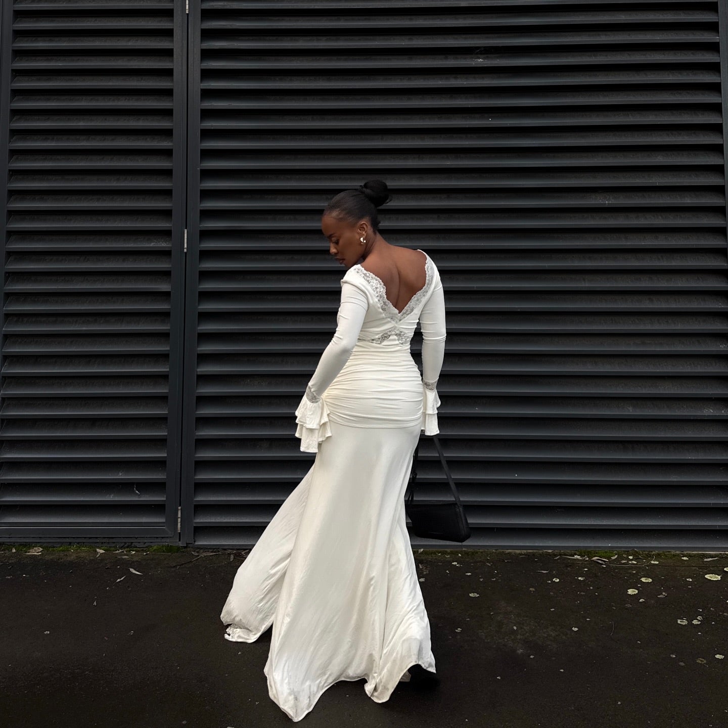 Woman in a white wedding dress standing in front of black shutters.