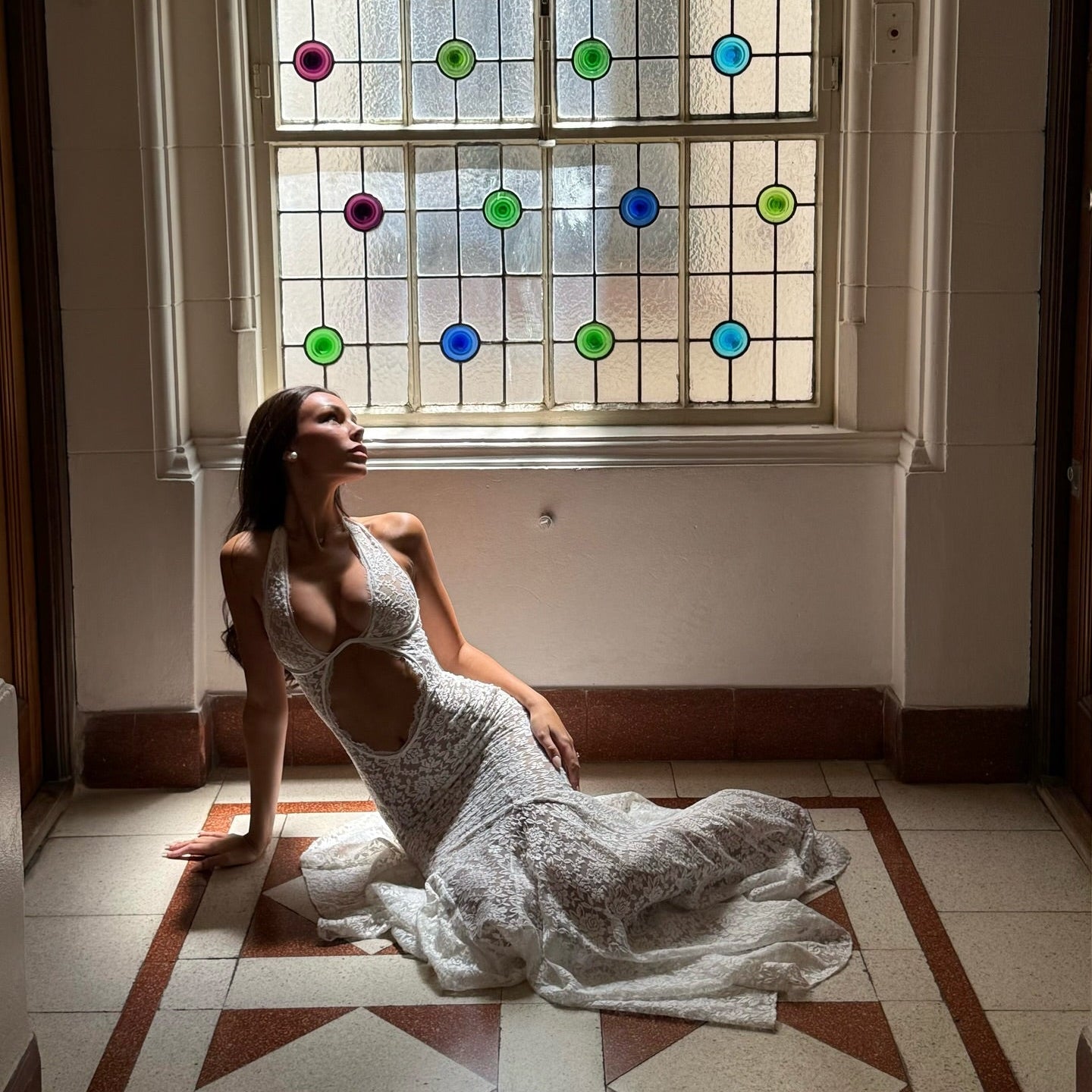 Woman in a white lace dress sitting on the floor in front of a stained glass window.