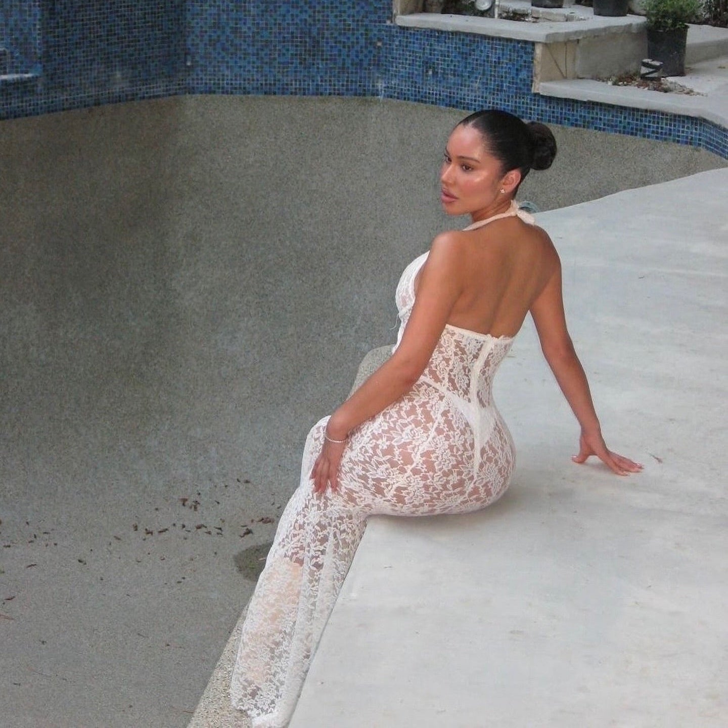 Woman in a white lace dress sitting by a poolside.