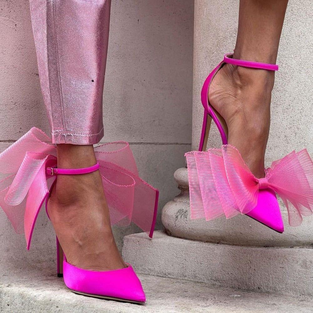 Pink high-heeled shoes with tulle bows worn by a person on a stone step.