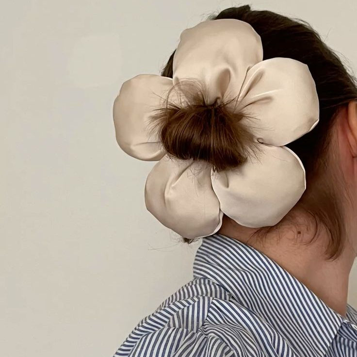 Person wearing a large beige flower-shaped hair accessory against a plain background
