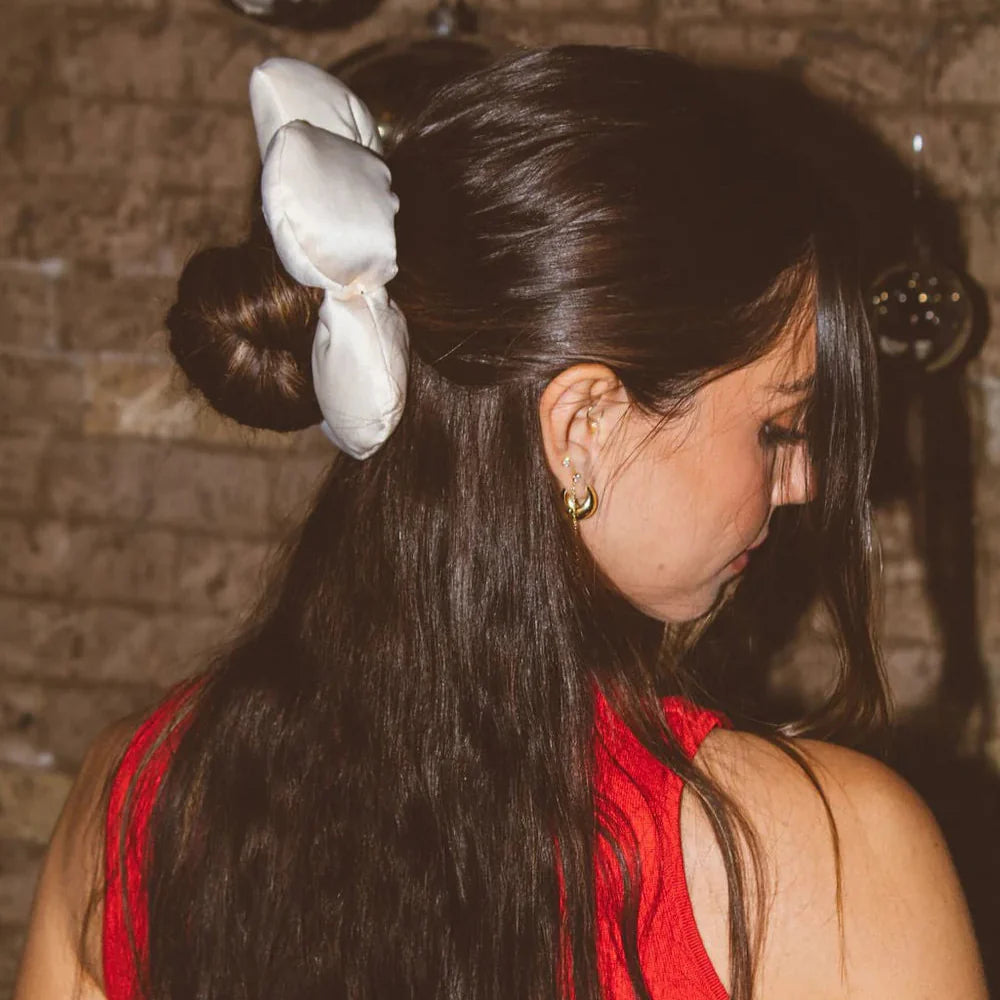 Woman with long dark hair styled in a bun with a white bow, wearing a red top.
