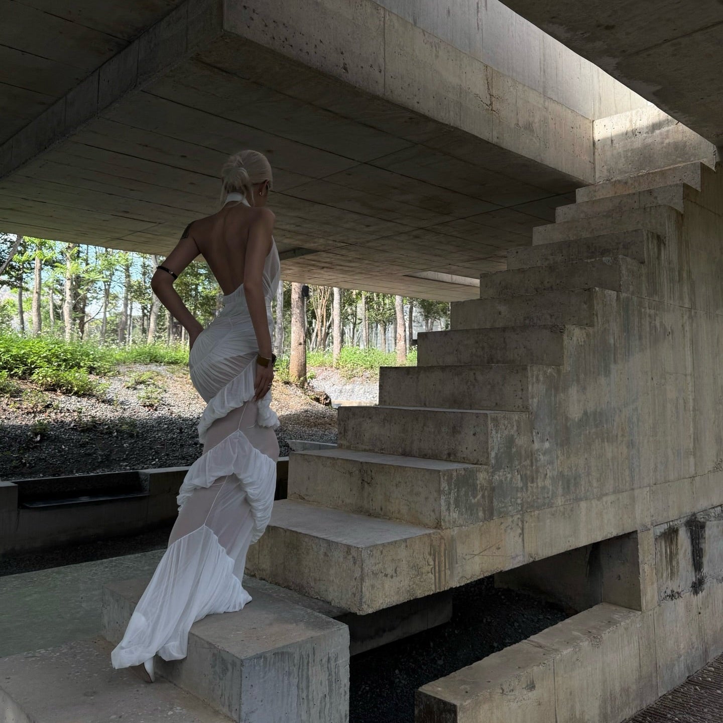 Woman in a white dress standing on concrete steps under a modern architectural structure.