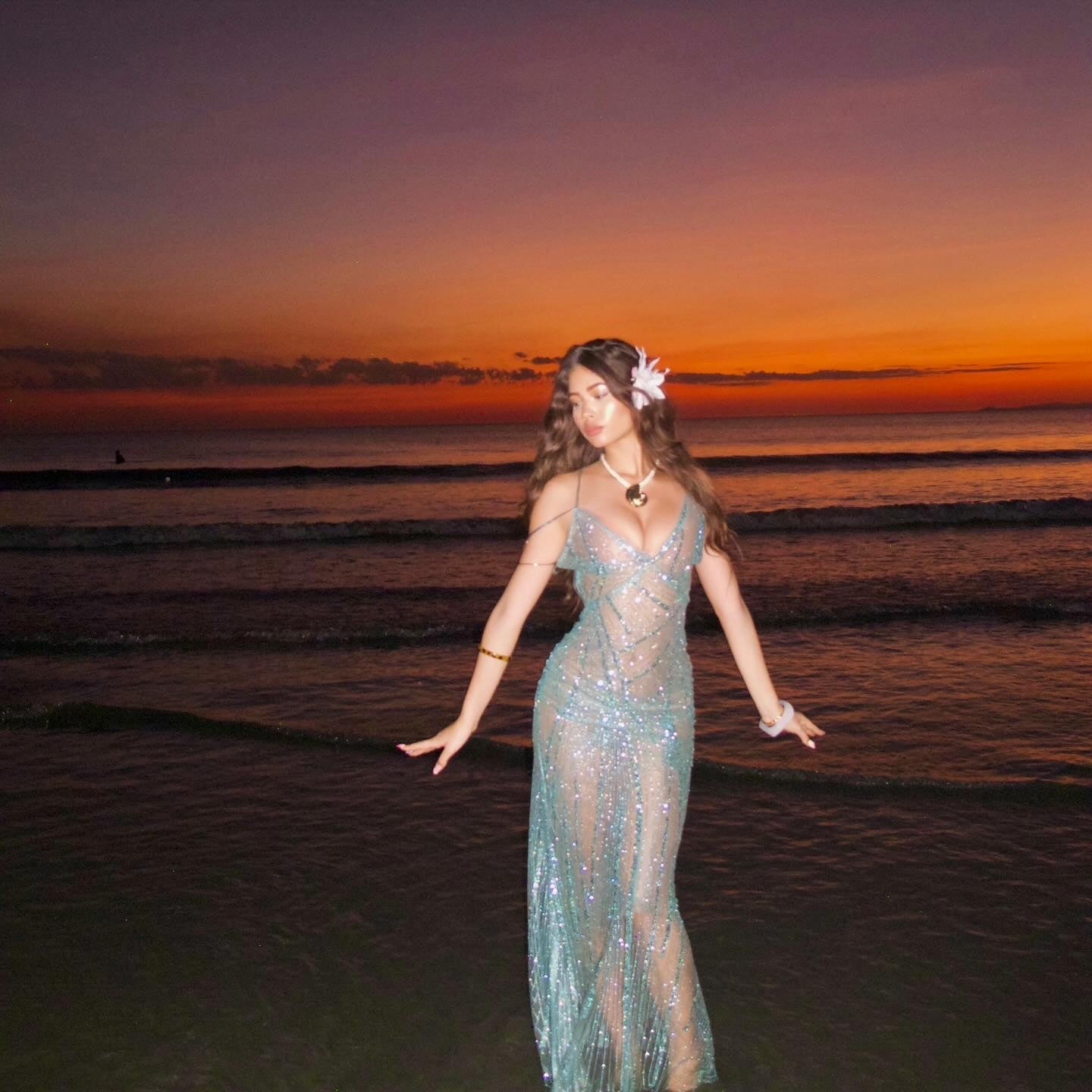 Woman in a sparkly dress standing on a beach at sunset