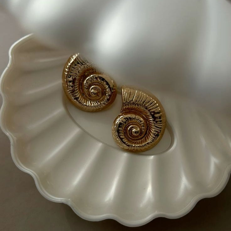 Gold spiral earrings on a white shell-shaped dish