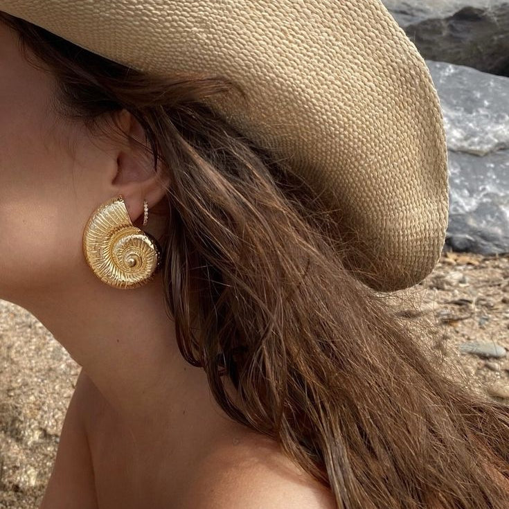 Close-up of a person wearing gold earrings with a beach background