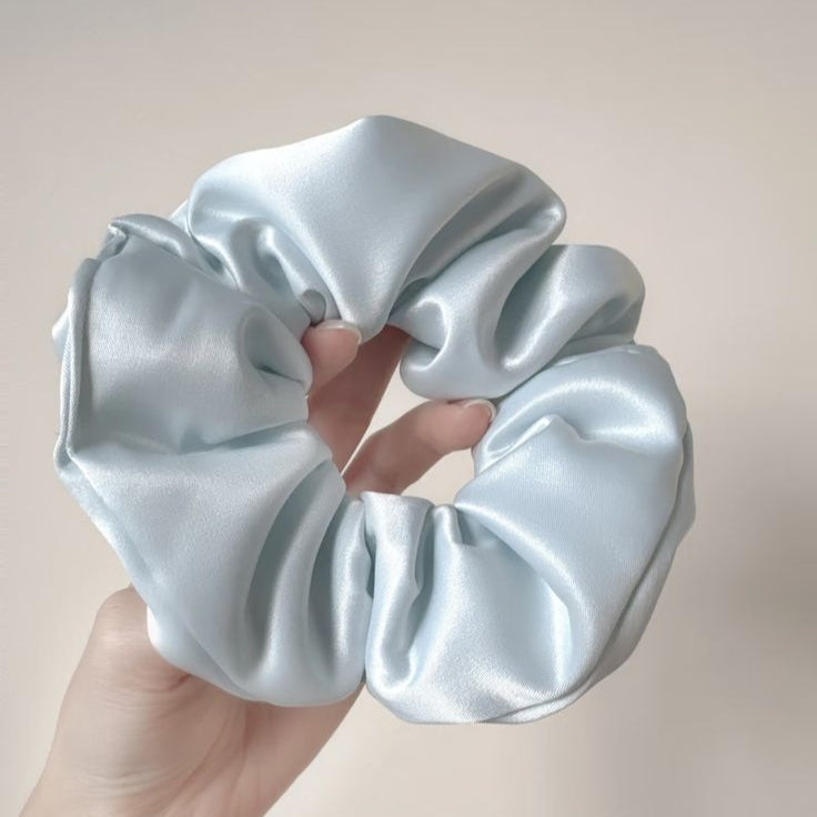 Light blue silk scrunchie held by a hand against a plain background
