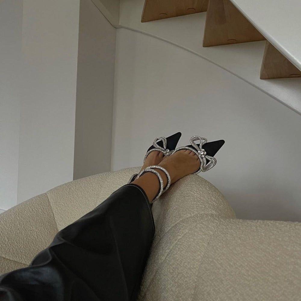 Person wearing black high-heeled shoes with decorative straps on a staircase.