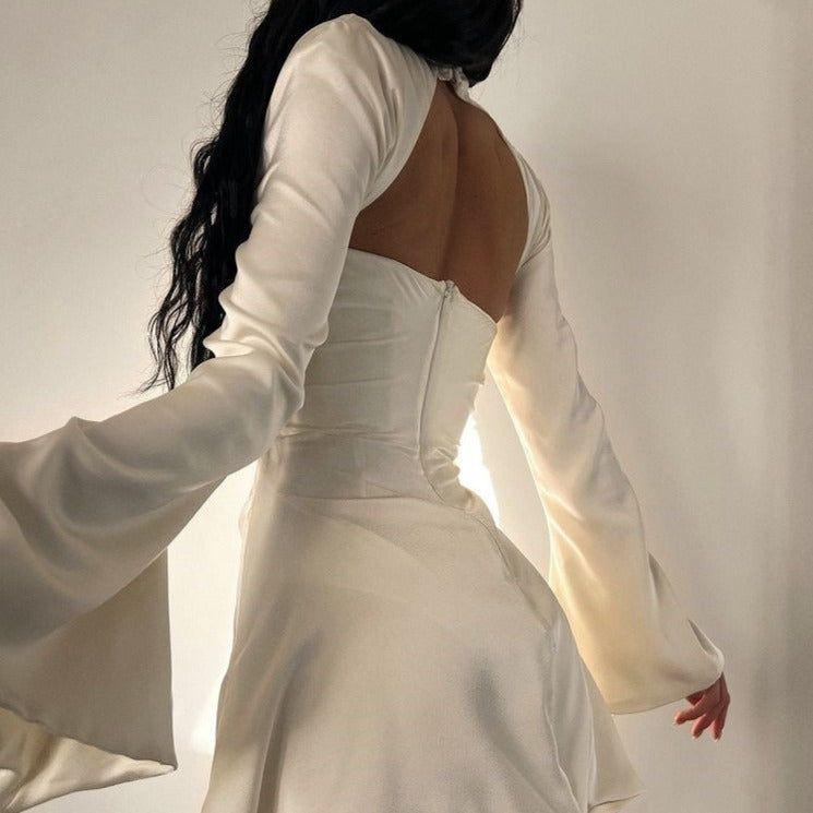 Woman wearing a white dress with long sleeves and an open back against a neutral background